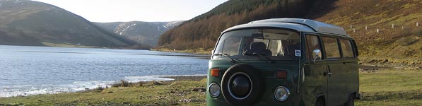 VW campervan by loch and mountains